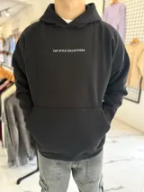 Canguro oversize negro con capucha y bolsillo tipo canguro. Presenta el texto "TOP STYLE COLLECTIONS" en el pecho y un estampado gráfico en la espalda con óvalos y texto en tonos celestes y blancos.