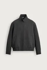 Cazadora de paño gris oscuro con corte regular fit, cuello alto, cierre frontal de cremallera y bolsillos de vivo en la cadera. Cuenta con bajo elástico y mangas largas con puños abotonados.