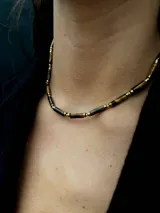 Collar de diseño delicado compuesto por cuentas cilíndricas de piedra natural ojo de tigre, intercaladas con pequeñas esferas doradas.