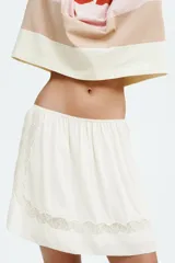 Minifalda holgada de viscosa color marfil con inserciones de encaje. Presenta cintura elástica con ribete de picot y frunces en todo el contorno, silueta ligeramente acampanada y dobladillo redondeado con abertura en cada lateral.