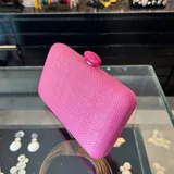 Clutch rectangular rígido de rafia sintética color fucsia, con cierre a tono y asa desmontable de cadena dorada para llevar al hombro.