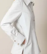 Camisa de cuero ovino italiano color blanco, de corte holgado, con cuello clásico, cierre frontal con broches metálicos, bolsillos laterales y puños con broches.