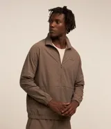 Campera deportiva Get Over de poliamida color marrón, con cuello alto, cierre frontal por cremallera, mangas largas con puños elásticos y etiqueta aplicada en el pecho.