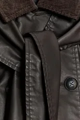 Capa de tejido encerado en color marrón oscuro, con diseño de cierre frontal cruzado con botones. Presenta un cuello de solapa en pana, solapa desmontable y mangas amplias con detalle de botón y trabilla.