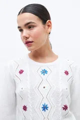 Sweater blanco de punto con bordado de flores azules, rojas y blancas. Tiene cuello redondo y mangas largas.