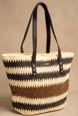 Bolso tipo tote de diseño trenzado con patrón de rayas en tonos marrones y beige, doble asa larga de material sintético oscuro y placa metálica con logo.