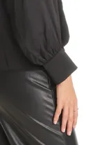 Blusa negra de acabado satinado con cuello alto fruncido, detalle de lazo para anudar y cierre lateral con botones. Presenta mangas largas estilo balloon con puños ajustados.