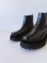 Botas negras de cuero con caña baja, cierre lateral con cremallera y suela track.