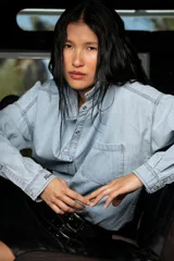 Camisa de jean liviano en tono celeste claro, con corte oversize, cuello clásico, cierre frontal con botones metálicos, bolsillo en el pecho y detalle de bordado en el puño.