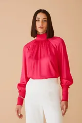Blusa fucsia de satén con cuello alto fruncido y mangas largas abullonadas con puños elásticos.