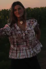 Camisa de corte peplum con volados en el escote y mangas cortas abullonadas. Presenta un estampado a cuadros en tonos rosados, verdes y marrones sobre fondo claro.