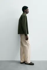 Sobrecamisa de hombre con cuello solapa, manga larga y cierre frontal de botonadura. Presenta un estampado de rayas verticales en tonos de verde oliva y verde oscuro. Incluye bolsillos plastrón en la cadera.