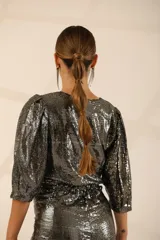 Mono corto plateado con lentejuelas, escote en V cruzado, mangas 3/4 abullonadas y corte asimétrico.