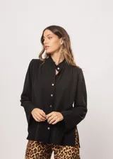 Camisa negra de cuello redondo con frunces y mangas largas con puños abiertos.