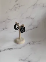 Aros tipo argolla trenzada en color negro con efecto de salpicaduras blancas, fabricados en arcilla polimérica.