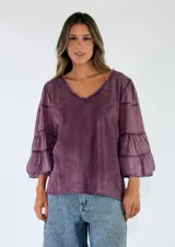 Blusa de algodón color gris oscuro con efecto gastado, mangas largas amplias con múltiples volados escalonados y terminaciones deshilachadas.