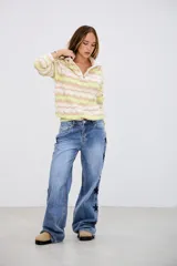 Sweater de punto con cuello alto y cierre frontal, de manga larga y diseño holgado. Presenta un patrón de ondas en colores blanco, beige y verde lima.