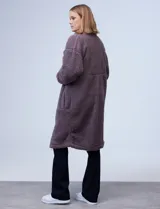 Campera larga de sherpa color negro, con cierre frontal y bolsillos laterales.