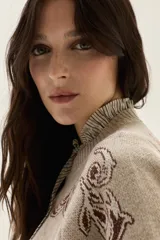 Sweater de tejido de punto color beige con diseño de arabescos en tonos marrones en hombros y mangas. Presenta cuello redondo con cordones decorativos y puños con textura acanalada.