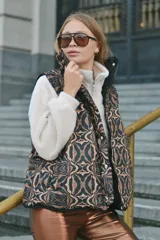 Chaleco marrón con estampado abstracto en tonos marrones y negros, con cierre frontal y broches a presión. Interior forrado con tela de peluche color crema y bolsillo interno.