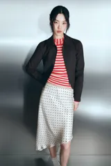 Falda midi de tejido satinado con estampado de lunares negros sobre fondo beige. Presenta un diseño de tiro medio con cintura elástica y un bajo con corte asimétrico.