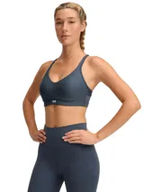 Top deportivo Under Armour Infinity Low 2.0 de sujeción ligera, color gris azulado. Presenta diseño tipo jersey con escote redondo, almohadillas moldeadas integradas y logo de la marca en el frente.