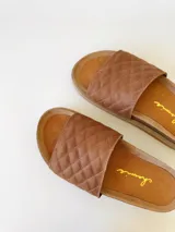 Sandalias chatas color camel, con diseño capitoneado en la tira superior. Fabricadas en cuero.