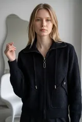 Campera de paño color marrón, con cuello alto, cierre frontal completo y cordones decorativos. Presenta bolsillos frontales con solapa y cierre a presión, y puños tejidos.