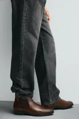 Bota Chelsea de cuero marrón, con punta fina y elásticos laterales oscuros. Posee un tirador trasero y un taco bajo y cuadrado.