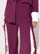 Pantalón sastrero largo color borgoña con recortes a contra tono y estampado floral en el delantero. En ambos laterales lleva flecos de tela base al tono.