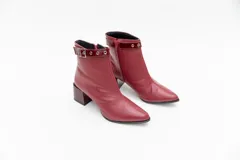 Botas de cuero negro, de caña baja, punta fina y taco cuadrado. Presentan un aplique charolado al tono, una correa con hebilla y ojales metálicos.