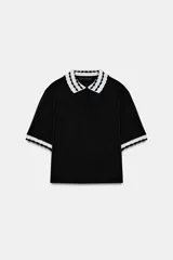 Top de tejido negro con cuello polo y bordes de manga cortos con diseño de ondas en blanco y negro. Tiene un cierre frontal de botones.