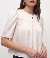 Blusa cropped de satén color crema, con cuello redondo, mangas cortas abullonadas con hombreras y detalle de fruncido en el frente.