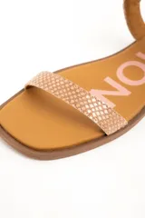 Sandalias planas de cuero color beige con estampado tipo animal print de serpiente texturado. Posee una tira delgada en la parte delantera y una tira ajustable con hebilla metálica alrededor del tobillo, sobre una suela plana y punta cuadrada.