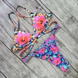 Top de bikini United Uy con diseño de estampado camuflado y flores grandes en tonos rosados, naranjas y celestes. Cuenta con copas triangulares, tirantes finos ajustables y tiras cruzadas en la parte inferior para atar en la espalda.