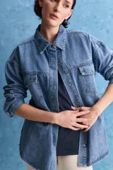 Sobrecamisa de denim de calce amplio y color azul, con cuello clásico, cierre frontal con broches metálicos y bolsillos delanteros con solapa.
