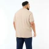 Remera polo de manga corta color beige, con cuello camisero sin botones y textura sutil de rayas verticales en relieve. Corte regular y diseño holgado.