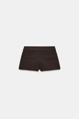 Bermudas de tiro medio color marrón con bolsillos en delantero y falsos bolsillos con solapa en espalda, de corte estructurado y cierre frontal con cremallera y ganchos metálicos.