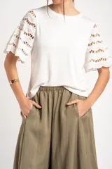 Remera blanca con mangas cortas abullonadas de encaje con diseño perforado, cuello redondo y corte oversize.