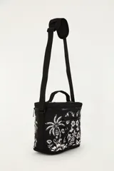 Bolso tipo lonchera o cooler de la marca Farm Rio, color negro con estampado floral y tropical en blanco. Cuenta con cierre superior con cremallera, bolsillo frontal con cierre, asa de mano superior y correa ajustable para colgar al hombro o cruzado.