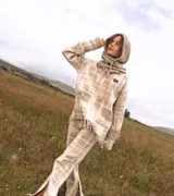 Sweater oversize de lana natural, color beige con estampado cuadrillé y detalles de flecos torneados. Incluye capucha integrada y logo "SM" bordado en el pecho.