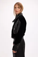 Campera crop de paño negro con recortes en cuero sintético, cuello alto con hebilla metálica, cierre frontal y hombreras marcadas.