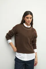 Sweater de tejido de punto color marrón, con cuello redondo y detalles de calados decorativos en el cuello y las mangas. Presenta un diseño de corte recto y manga larga.