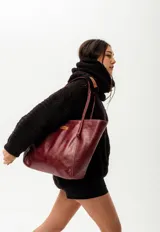 Cartera de cuero color bordó, tipo tote bag, con doble asa de hombro y detalle de nudo en una de ellas. Incluye doble bolsillo y colgante interno para llaves.