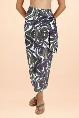 Pareo largo de diseño envolvente con nudo lateral, confeccionado en tejido fresco con estampado de motivos orgánicos en tonos verde y violeta sobre fondo blanco.