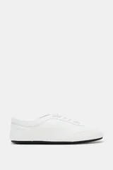 Zapatilla deportiva estilo blucher de color blanco, con cordones del mismo tono, pespuntes decorativos y suela plana con base negra.