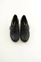 Zapato de cuero negro con cierre de velcro ancho y costuras pespunteadas a contratono.