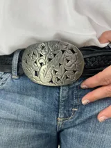 Cinturón negro de cuero trenzado con hebilla ovalada de metal plateado con diseño floral calado.