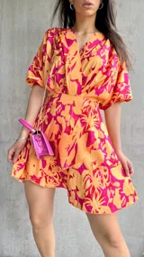 Vestido corto color naranja con estampado floral fucsia, escote cruzado, mangas cortas abullonadas y falda con volados.