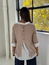 Sweater de punto rosa claro con diseño de capas, que incluye una camisa blanca debajo y un pañuelo a juego con detalles de encaje y flecos en el ruedo.